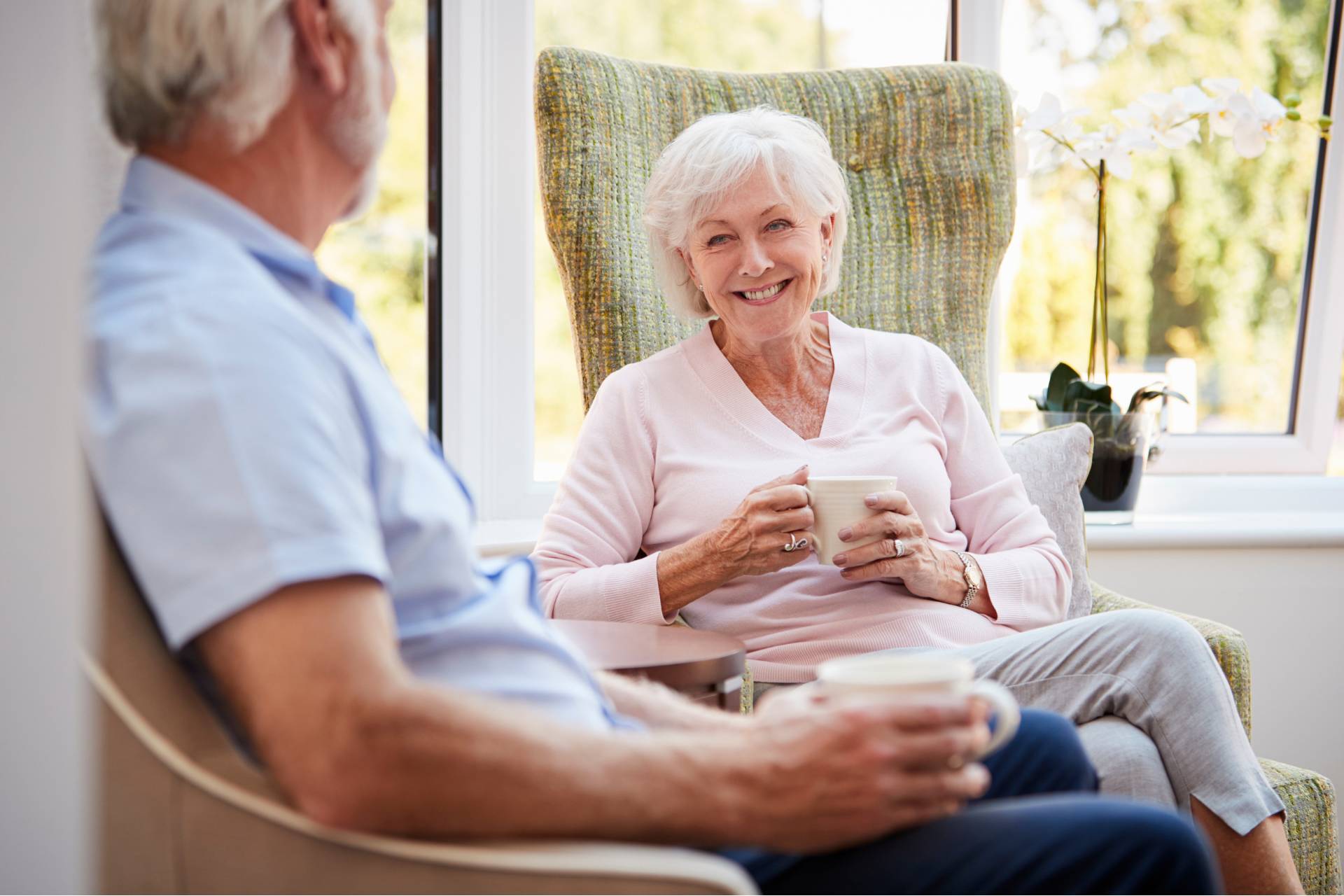 A senior woman holding a cup of coffee and smiling at a senior man
