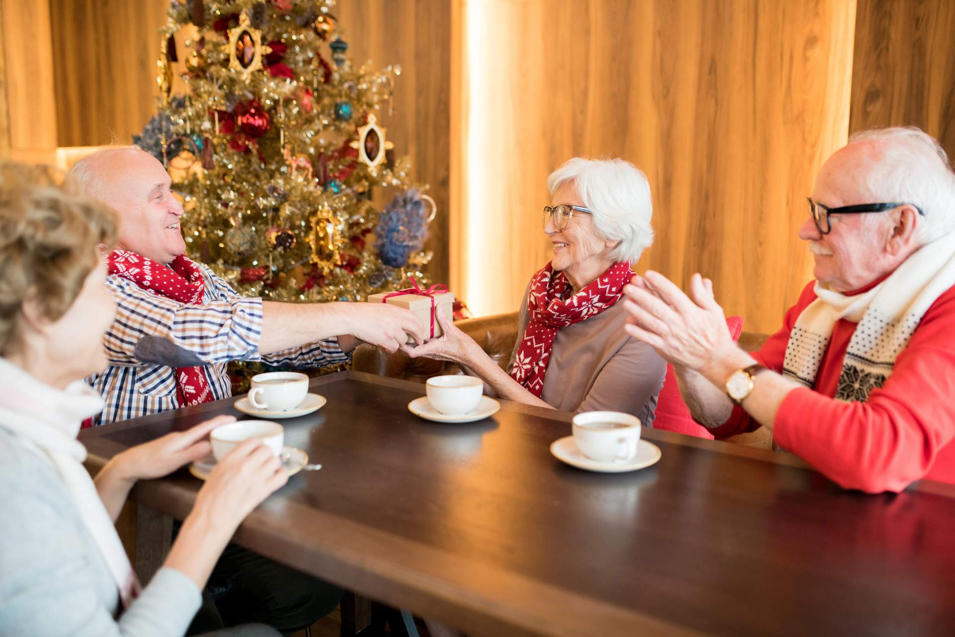 Seniors sitting at a table drinking hot chocolate together, in front of a Christmas tree.